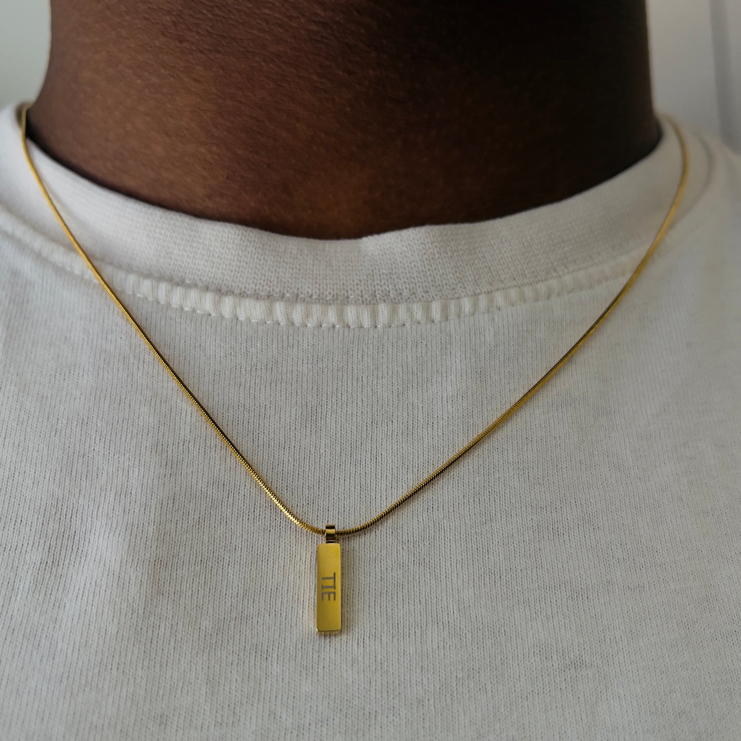 Detalhe do pendente quadrado dourado em aço inoxidável 316L do colar minimalista da The Iron Essence